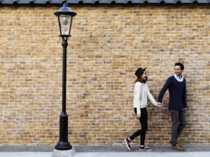 couple holding hands, walking in front of a brick wall